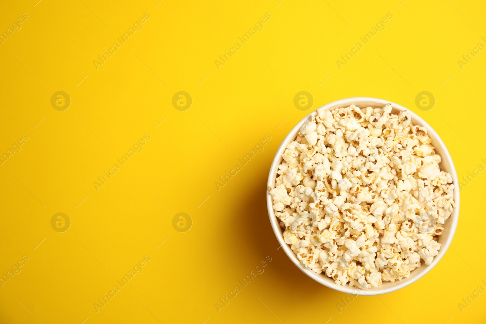 Photo of Paper bucket with tasty fresh popcorn on color background, top view