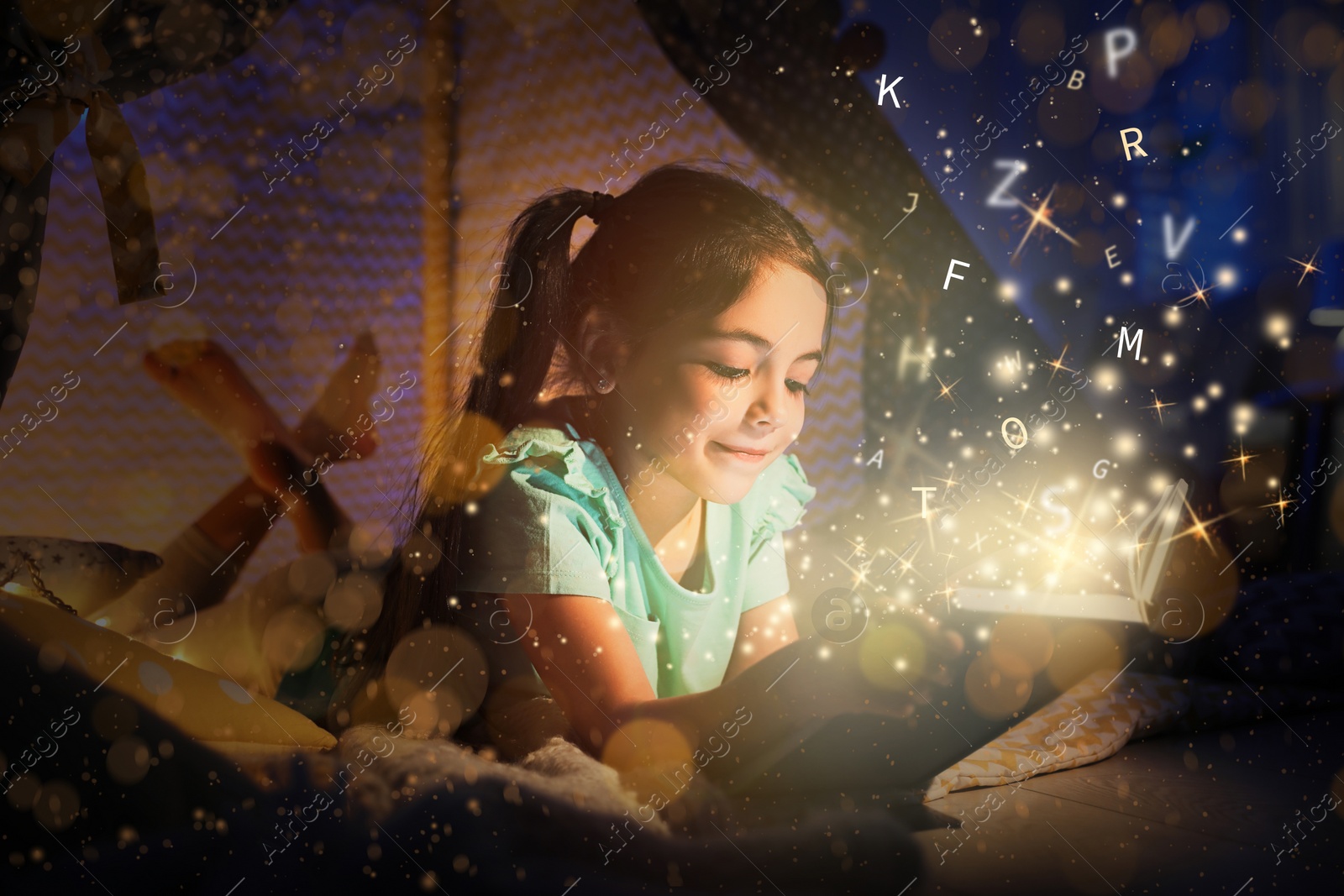 Image of Girl reading shiny magic book with letters flying over it in play tent at home