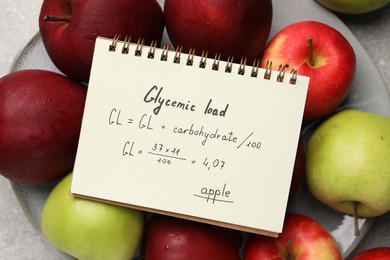 Photo of Notebook with calculated glycemic load for apples and fresh fruits on table, top view