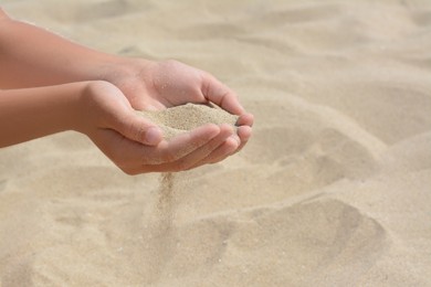 Photo of Child pouring sand from hands on beach, closeup with space for text. Fleeting time concept
