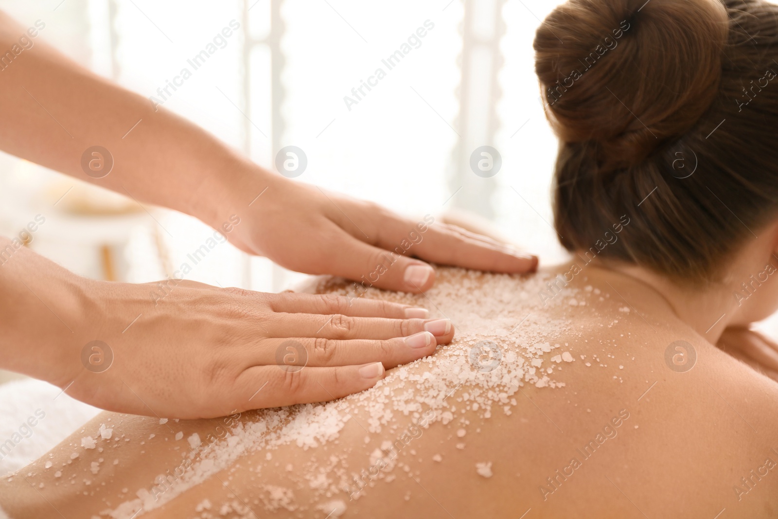 Photo of Young woman having body scrubbing procedure with sea salt in spa salon, closeup