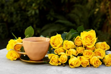 Photo of Cup of drink and beautiful yellow roses on light table outdoors, space for text