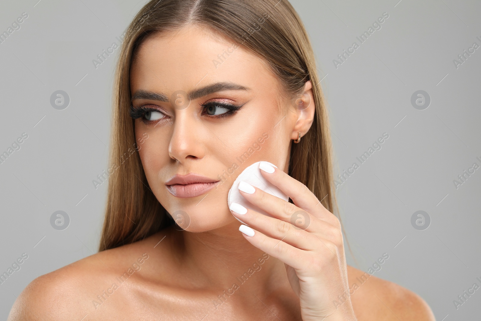 Photo of Beautiful woman removing makeup with cotton pad on grey background