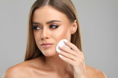 Beautiful woman removing makeup with cotton pad on grey background