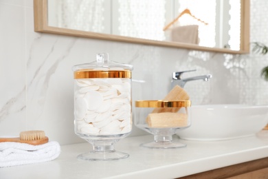 Photo of Jars with cotton pads and loofah sponges on bathroom countertop