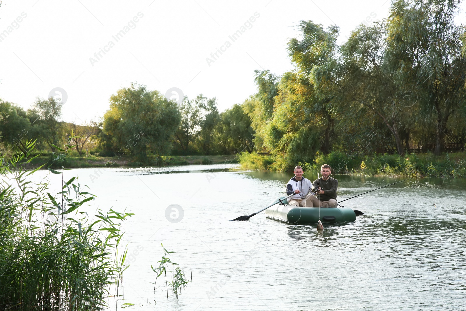 Photo of Friends fishing from boat on river. Recreational activity