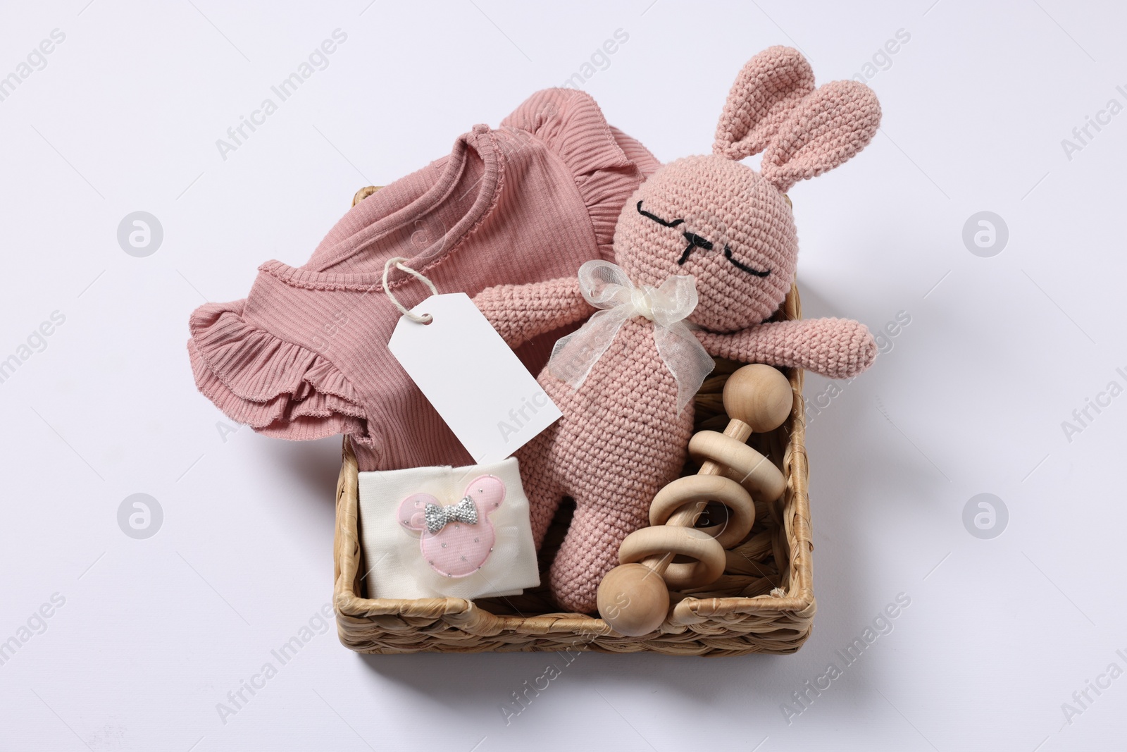 Photo of Different baby accessories, clothes and blank card in wicker box on white background, top view