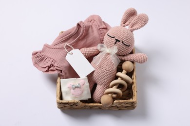 Photo of Different baby accessories, clothes and blank card in wicker box on white background, top view