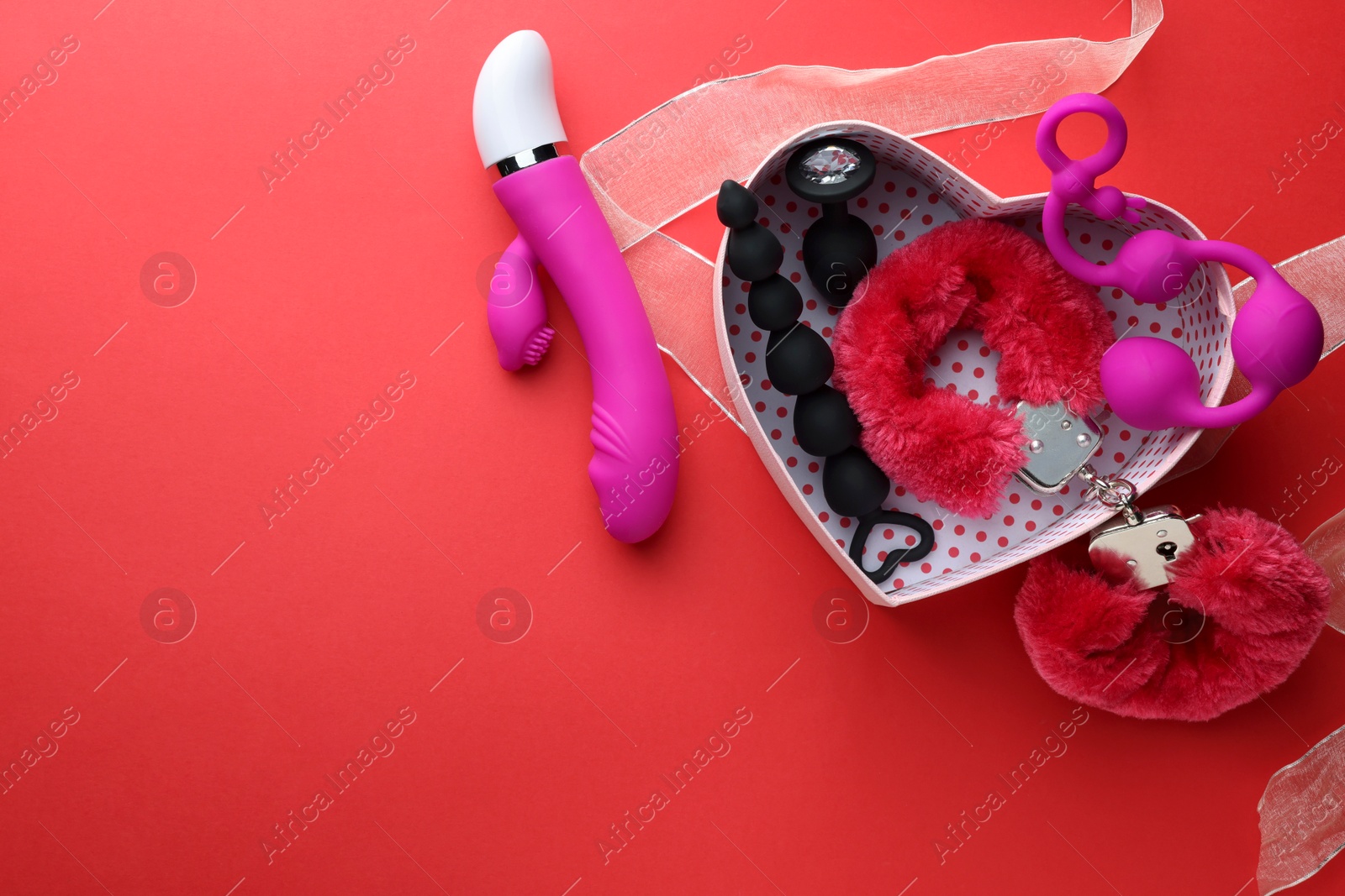 Photo of Gift box with different sex toys on red background, flat lay. Space for text