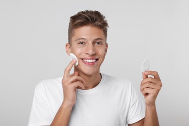 Photo of Handsome man cleaning face with cotton pad on light background