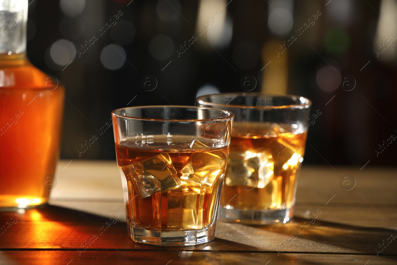 Photo of Glasses of whiskey with ice on wooden table in bar, space for text