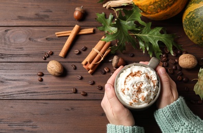 Woman with cup of tasty pumpkin spice latte at wooden table, top view. Space for text