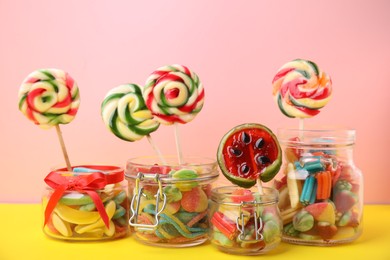 Photo of Tasty colorful candies in glass jars on yellow table against pink background