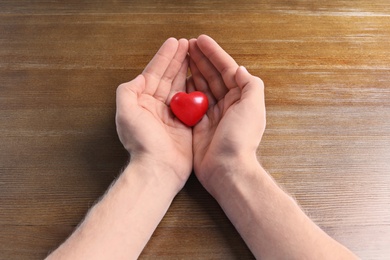 Photo of Man holding small red heart on wooden table. Heart attack concept