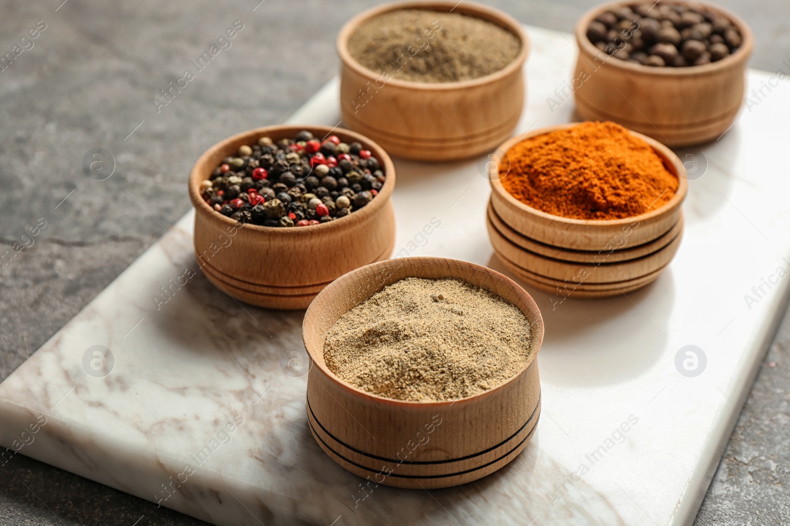 Photo of Marble board with different types of pepper in bowls on table