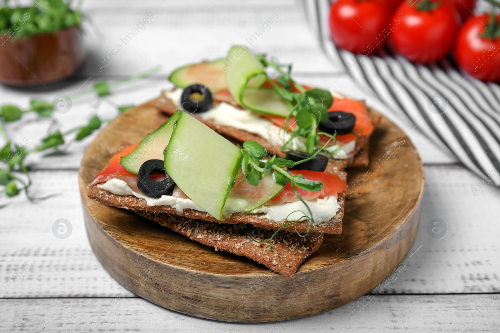 Photo of Tasty rye crispbreads with salmon, cream cheese and vegetables on white wooden table, closeup