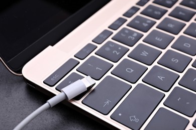 USB cable with lightning connector and laptop on black table, closeup