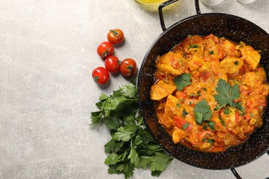 Photo of Delicious chicken curry in frying pan, parsley and tomatoes on light grey table, flat lay. Space for text