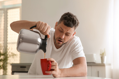 Photo of Sleepy man pouring coffee into cup at home in morning