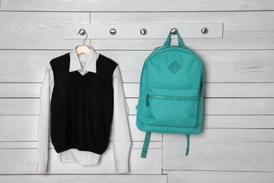 Photo of Shirt, backpack and jumper hanging on white wooden wall. School uniform