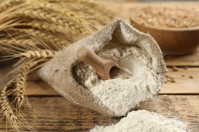 Photo of Sack of flour with wooden scoop and wheat ears on wooden table