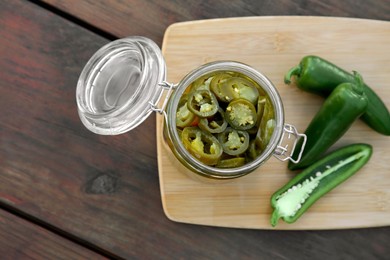 Photo of Fresh and pickled green jalapeno peppers on wooden table, top view