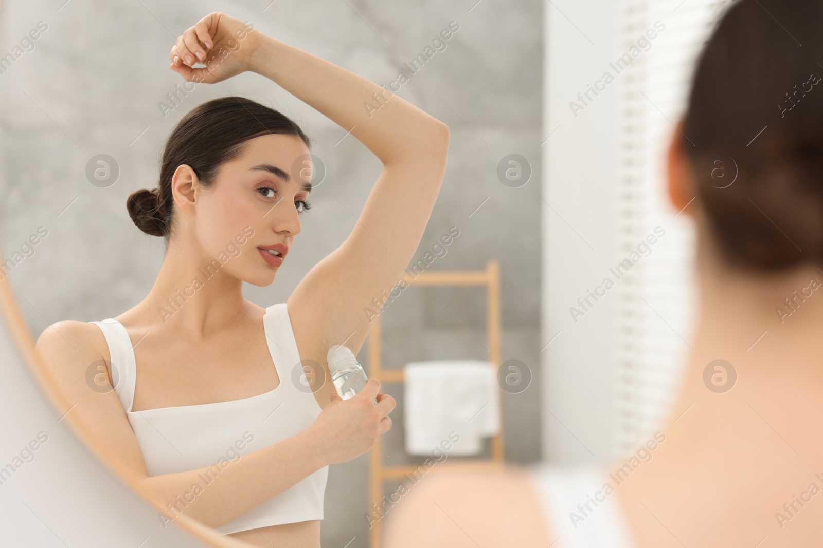 Photo of Beautiful woman applying deodorant near mirror in bathroom