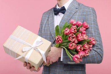 Photo of Man with beautiful bouquet and present on pink background, closeup