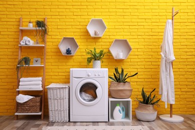 Photo of Laundry room interior with modern washing machine near yellow brick wall