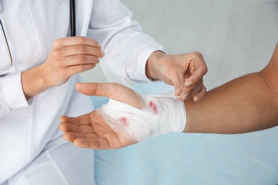 Female doctor applying bandage on young man's hand in clinic, closeup. First aid