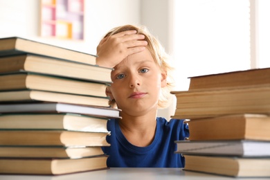 Photo of Emotional little boy at table with books. Doing homework
