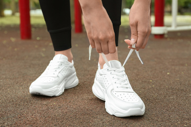 Woman tying laces of stylish sneakers outdoors, closeup