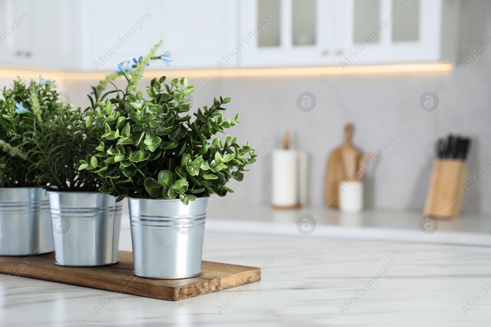 Photo of Different artificial potted herbs on white marble table in kitchen, space for text