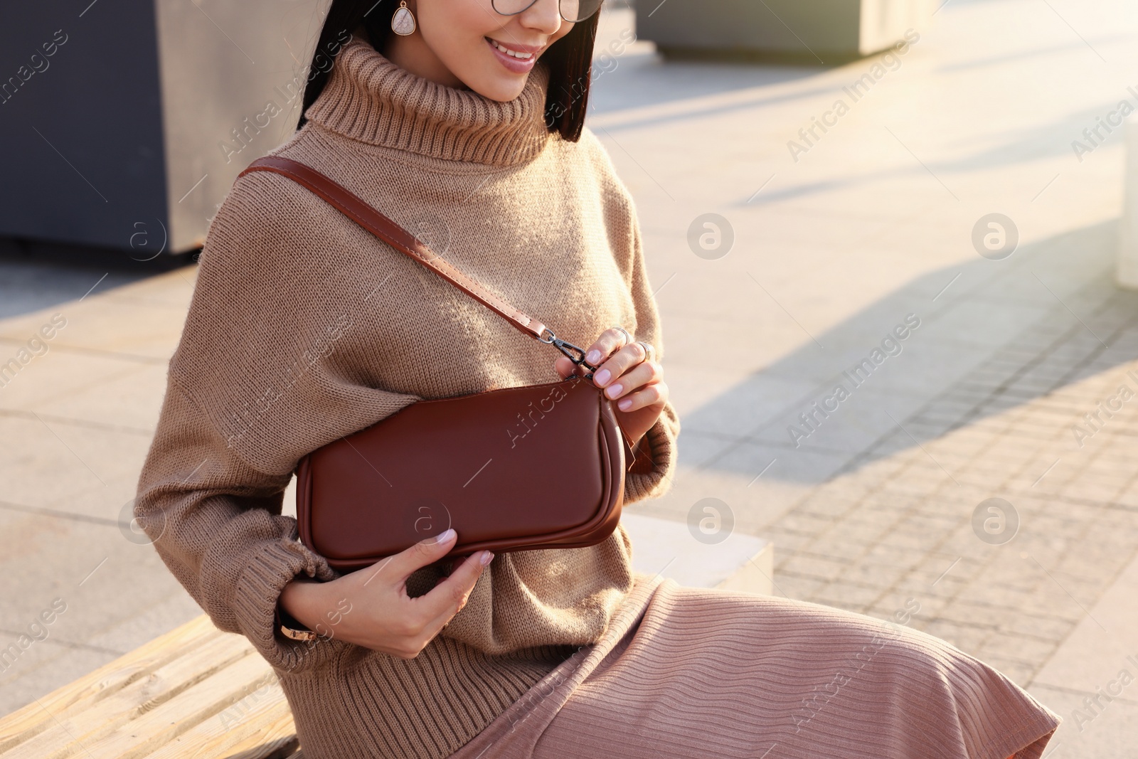 Photo of Fashionable young woman with stylish bag on bench outdoors, closeup