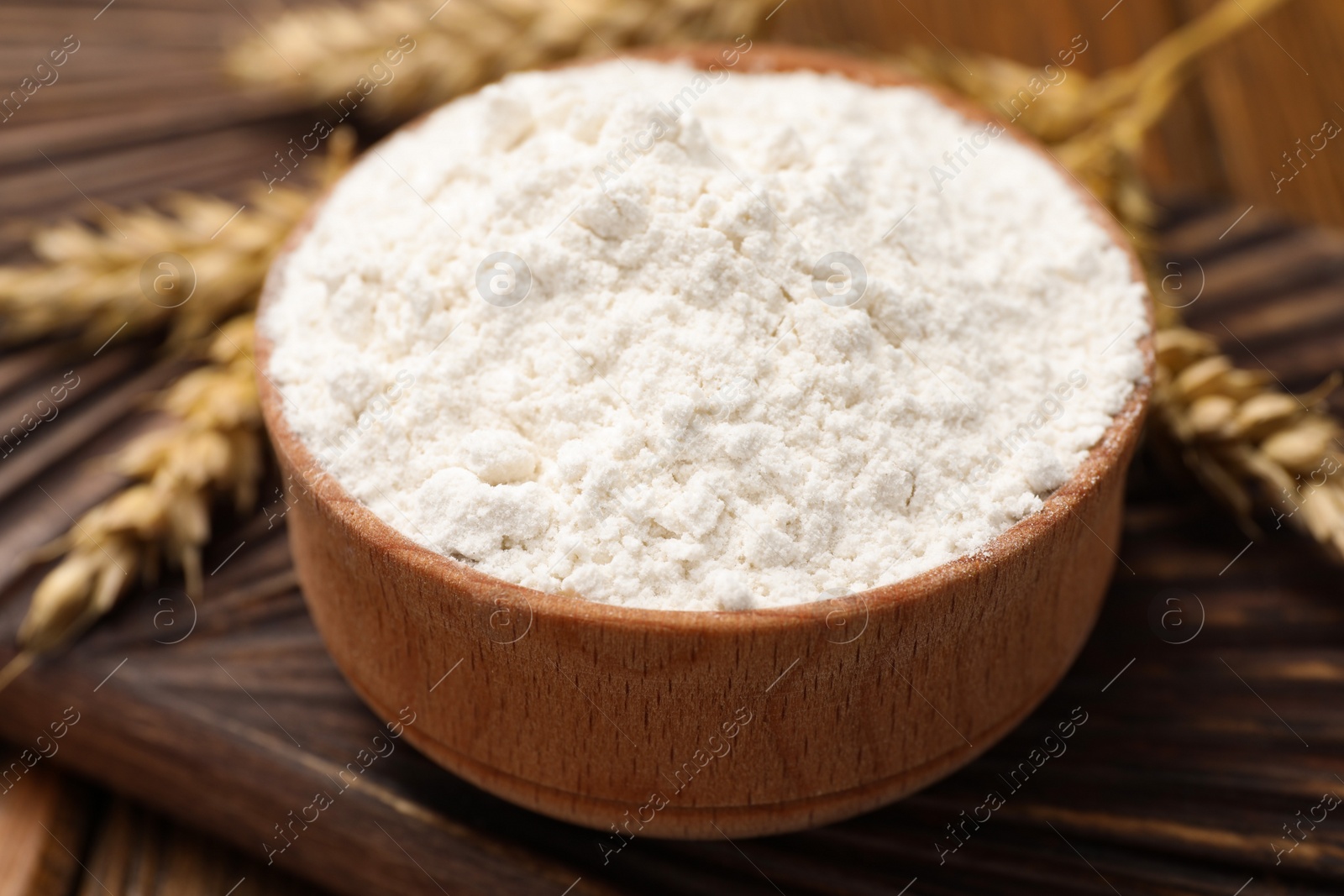 Photo of Bowl of organic wheat flour on wooden table, closeup