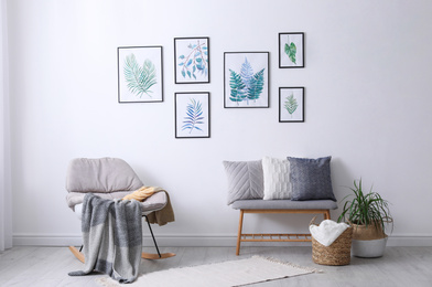 Photo of Beautiful paintings of tropical leaves on white wall in living room interior