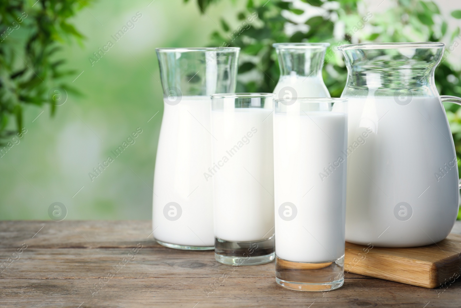 Photo of Glassware with fresh milk on wooden table against blurred background