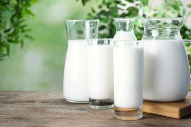 Photo of Glassware with fresh milk on wooden table against blurred background
