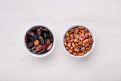 Photo of Bowls with different types of beans on white wooden table, flat lay