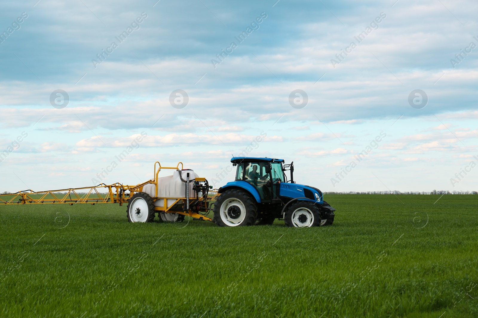 Photo of Tractor spraying pesticide in field on spring day. Agricultural industry