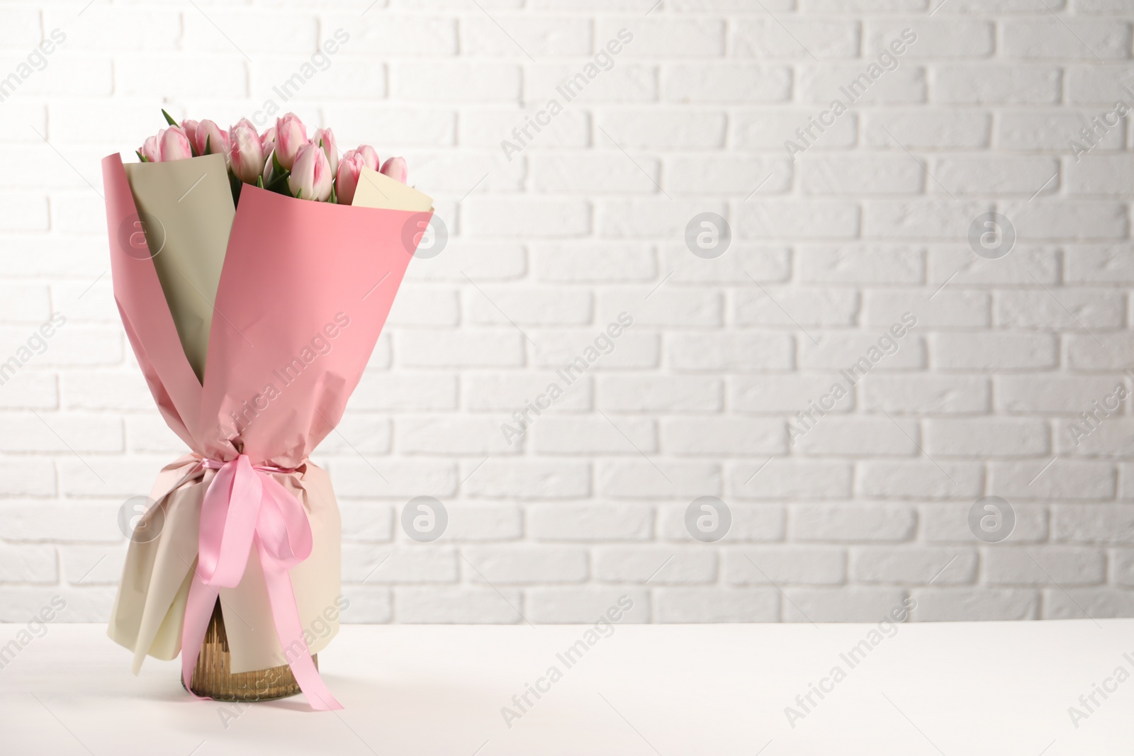 Photo of Beautiful bouquet of fresh pink tulips on table near white brick wall. Space for text