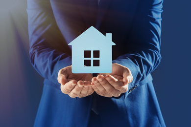 Image of Home security concept. Man holding house on dark background, closeup