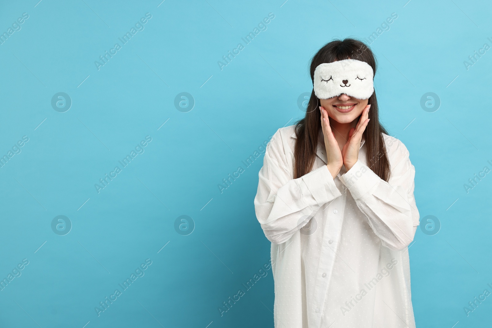 Photo of Woman in pyjama and sleep mask on light blue background, space for text