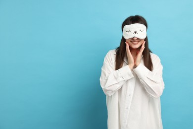 Woman in pyjama and sleep mask on light blue background, space for text