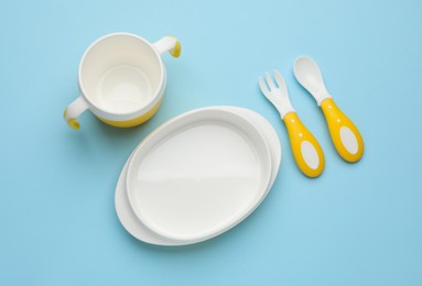 Set of plastic dishware on light blue background, flat lay. Serving baby food