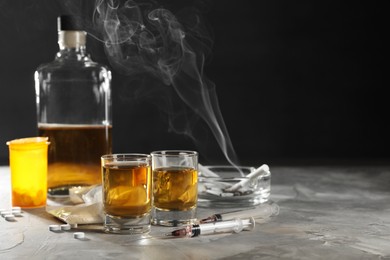 Photo of Alcohol and drug addiction. Whiskey in glasses, syringes, pills and cocaine on grey table, space for text