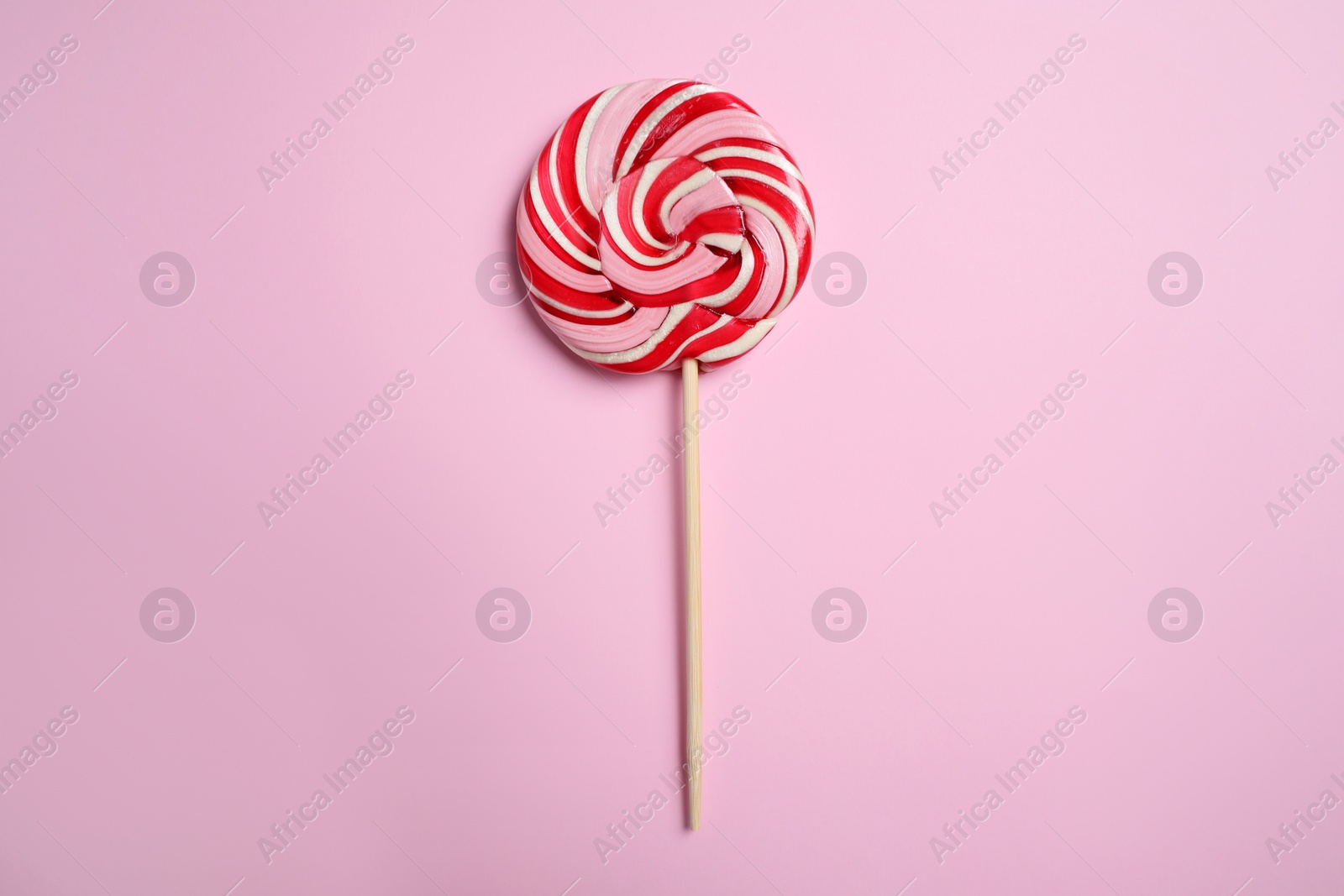 Photo of Stick with colorful lollipop swirl on pink background, top view