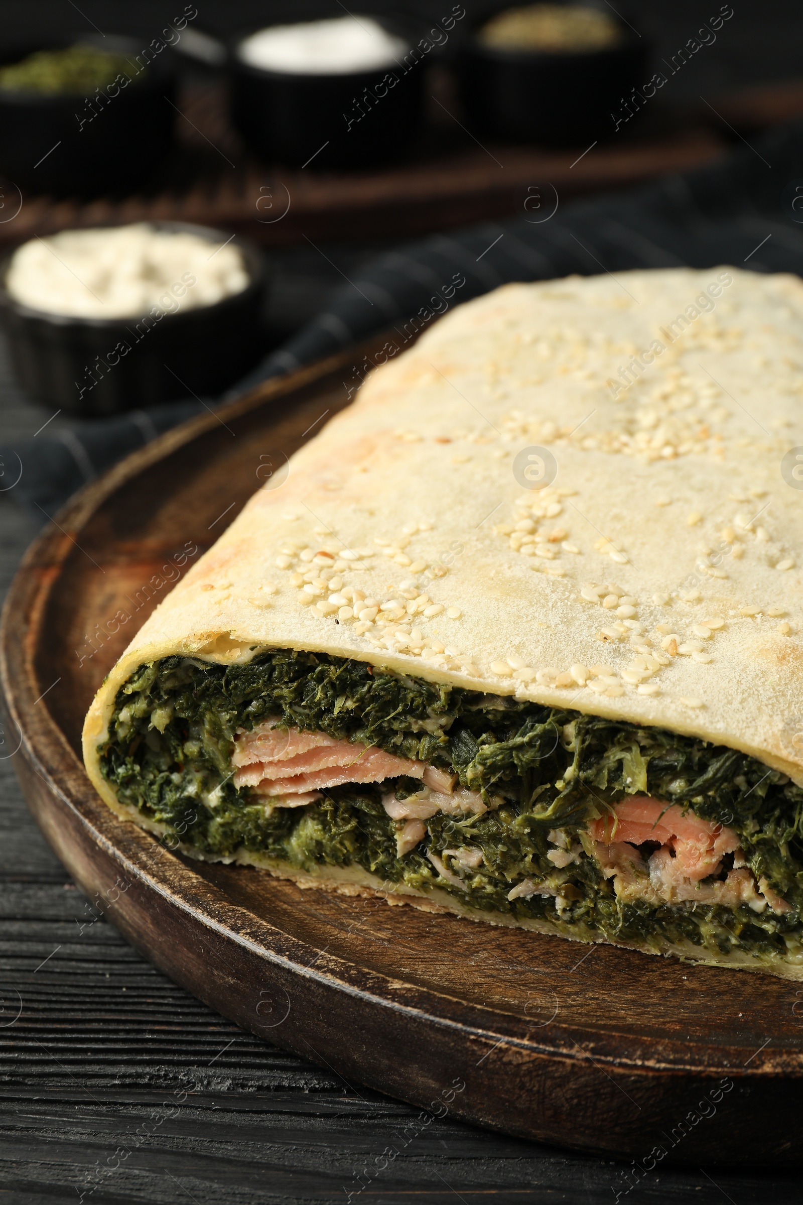 Photo of Tasty strudel with salmon and spinach on black wooden table, closeup