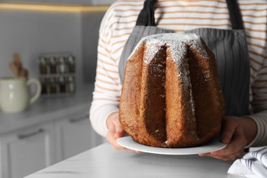 Photo of Woman holding delicious Pandoro cake decorated with powdered sugar in kitchen, closeup and space for text. Traditional Italian pastry