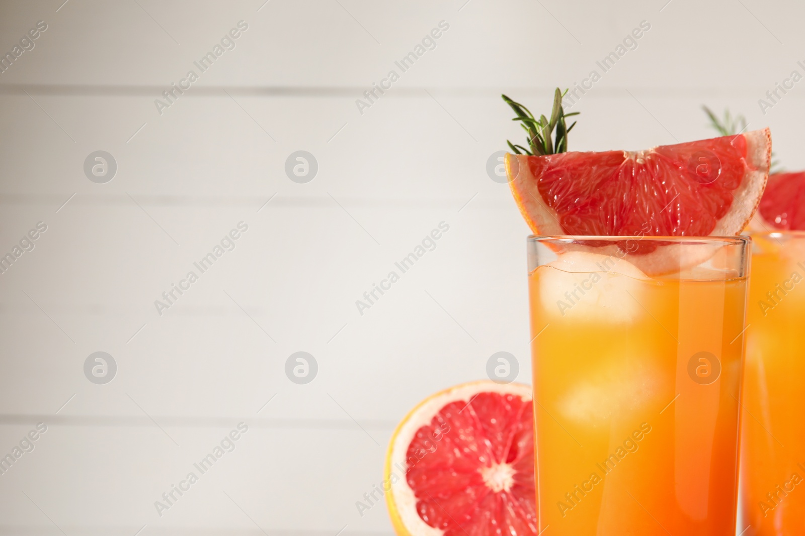 Photo of Tasty grapefruit drink with ice, rosemary and slices of fresh fruits in glasses on white background, closeup. Space for text